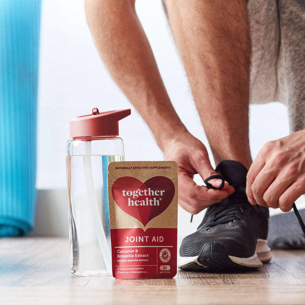 Mann bindet seinen Turnschuh und hat eine Wasserflasche und eine Tüte Together Health Joint Aid neben sich stehen