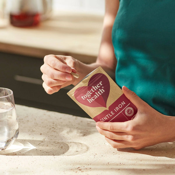Frau hält Together Health Gentle Iron Tüte in den Händen und nimmt eine Kapsel heraus